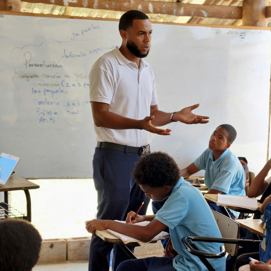 A teacher leads a lesson with attentive students in an informal classroom setting.